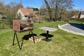 En enkel utegrill placerad på en gräsplätt, med en byggnad i sten som syns i bakgrunden.
