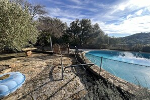 A stone pool with a metal ladder, surrounded by trees and a view of a hilly landscape. - Holiday home with 3 bedrooms (Cabrials (Aumelas))