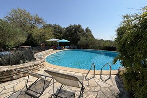 A swimming pool with a stone border, a lounge chair, and a blue umbrella. - Holiday home with 3 bedrooms (Cabrials (Aumelas))
