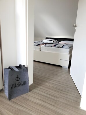 A bedroom with a bed, a white wardrobe, and a grey bag on the floor. - Apartment 'Nordseeperle Strandkorb Am Strand' with Balcony and Wi-Fi (Wangerland)