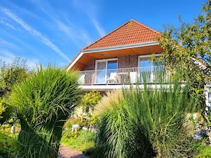 A house with a red-tiled roof, a balcony with white railings, and lush greenery around. - Apartment 'Nordseeperle Strandkorb Am Strand' with Balcony and Wi-Fi (Wangerland)