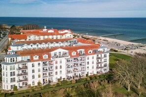 Ein großes, mehrstöckiges Hotel mit rotem Ziegeldach in Strandnähe mit einer Promenade.