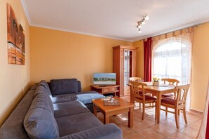 Ein Wohnzimmer mit einer Couch, einem Fernseher, einem Esstisch mit Stühlen und einem Schrank.