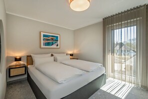 Ein Hotelzimmer mit einem Bett, zwei Nachttischen, einer Lampe, einem Bild an der Wand und einem Fenster mit Vorhängen.