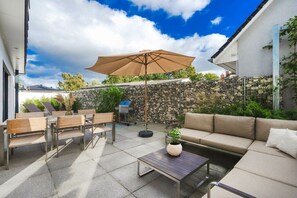 An outdoor patio area with a stone wall, a wooden bench, a sofa, a table, and a large umbrella. - Holiday apartment with 1 bedroom (Lubmin)