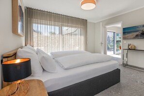 A modern hotel room with a bed, a nightstand, a lamp, and a view of the outdoors. - Holiday apartment with 1 bedroom (Lubmin)