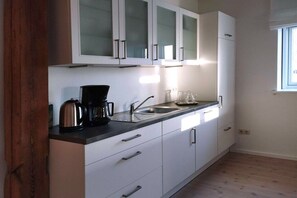A modern kitchen with white cabinets, a stainless steel coffee maker, and a window providing natural light. - Sonnenhof by the sea (Osterhever)