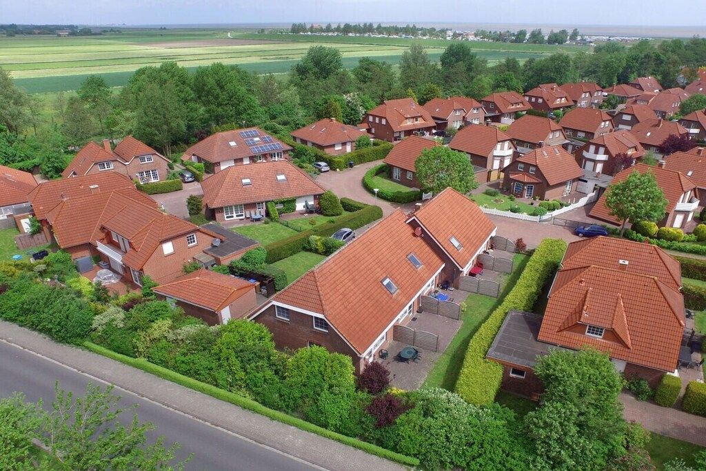A residential area with houses featuring red-tiled roofs, surrounded by greenery and a road.