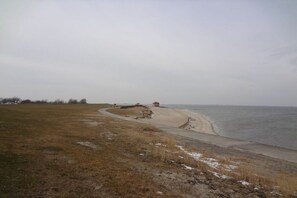 A coastal landscape with a sandy beach, a grassy area, and a red structure near the water. - Holiday home in Hooksiel with swimming pool (Hooksiel)