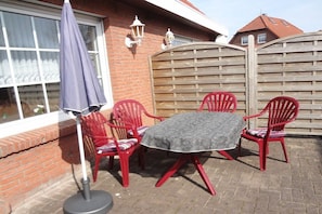 An outdoor patio with a table and four chairs, a blue umbrella, and a brick wall. - Holiday home in Hooksiel with swimming pool (Hooksiel)
