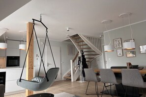 A modern kitchen with a hanging chair, a dining area with chairs, and a staircase. - Holiday apartment with 1 bedroom (Langeoog)