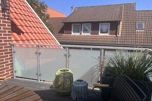 A balcony with a glass railing, a wooden deck, and potted plants. - Holiday apartment with 1 bedroom (Langeoog)