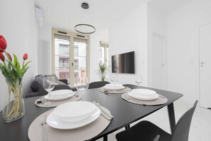 A dining area with a table set for four, a potted plant, and a view of the outside balcony. - Warsaw | Żelazna 54 | Modern Studio | Air Conditioning (Warszawa)