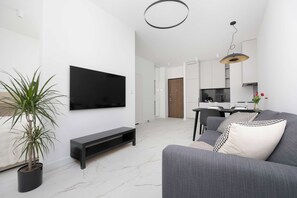 Een moderne woonkamer met een flatscreen televisie, een grijze bank, een zwarte tv-meubel en een potplant.