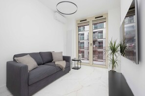 A modern living room with a grey sofa, a small side table, and a potted plant. - Warsaw | Żelazna 54 | Modern Studio | Air Conditioning (Warszawa)
