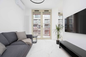 A modern living room with a grey sofa, a flat-screen TV, and a potted plant. - Warsaw | Żelazna 54 | Modern Studio | Air Conditioning (Warszawa)