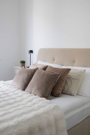 A neatly made bed with a white duvet and multiple pillows, a bedside lamp, and a small potted plant on a nightstand. - Warsaw | Żelazna 54 | Modern Studio | Air Conditioning (Warszawa)