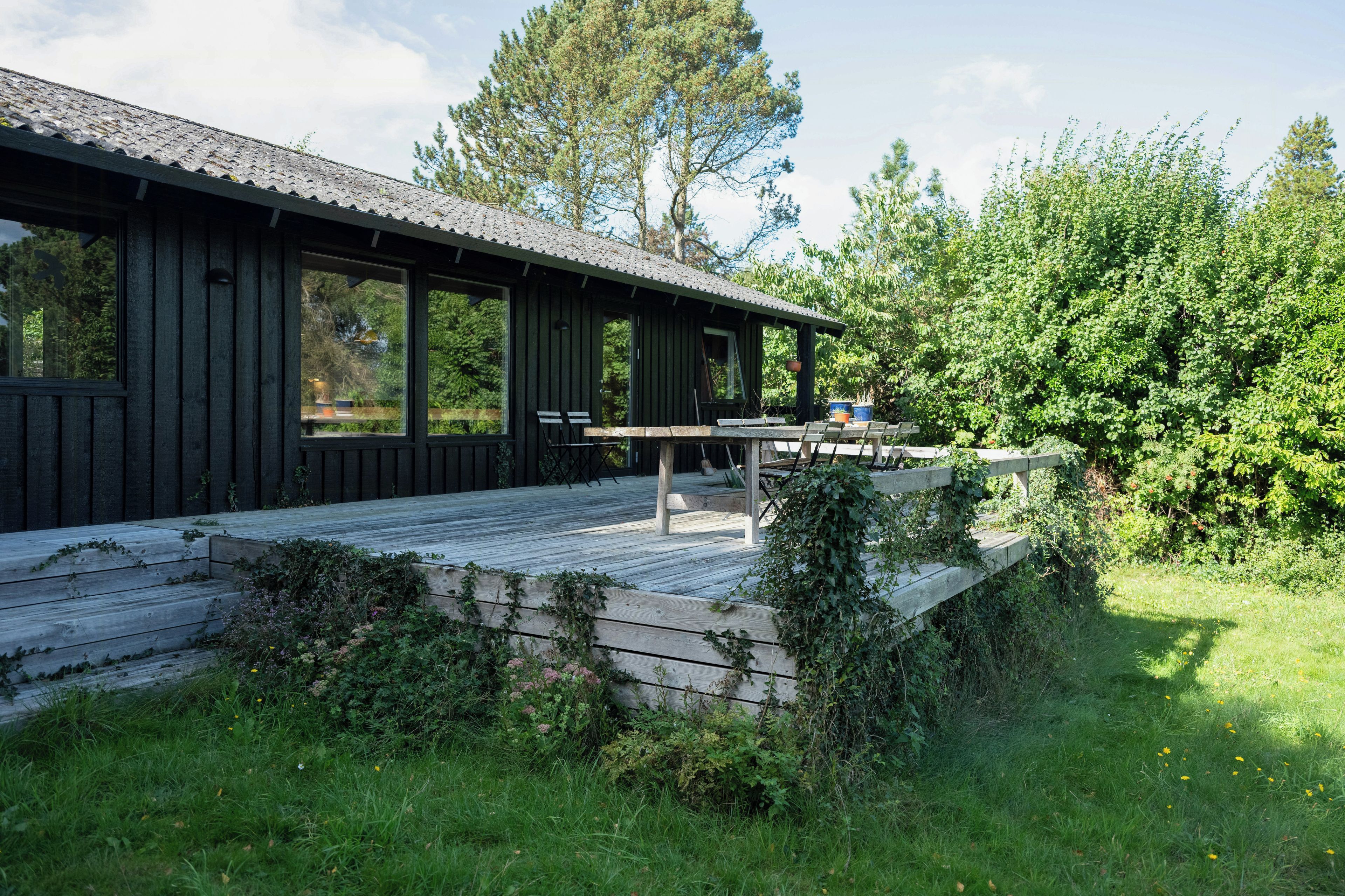 A wooden cabin with a deck, large windows, and a view of the surrounding greenery.