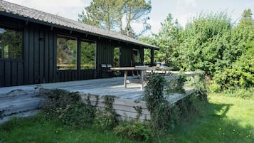 A wooden cabin with a deck, large windows, and a view of the surrounding greenery.