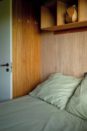 Une chambre à coucher avec une armoire en bois, un lit avec une literie blanche et une étagère sur laquelle est posé un objet décoratif.