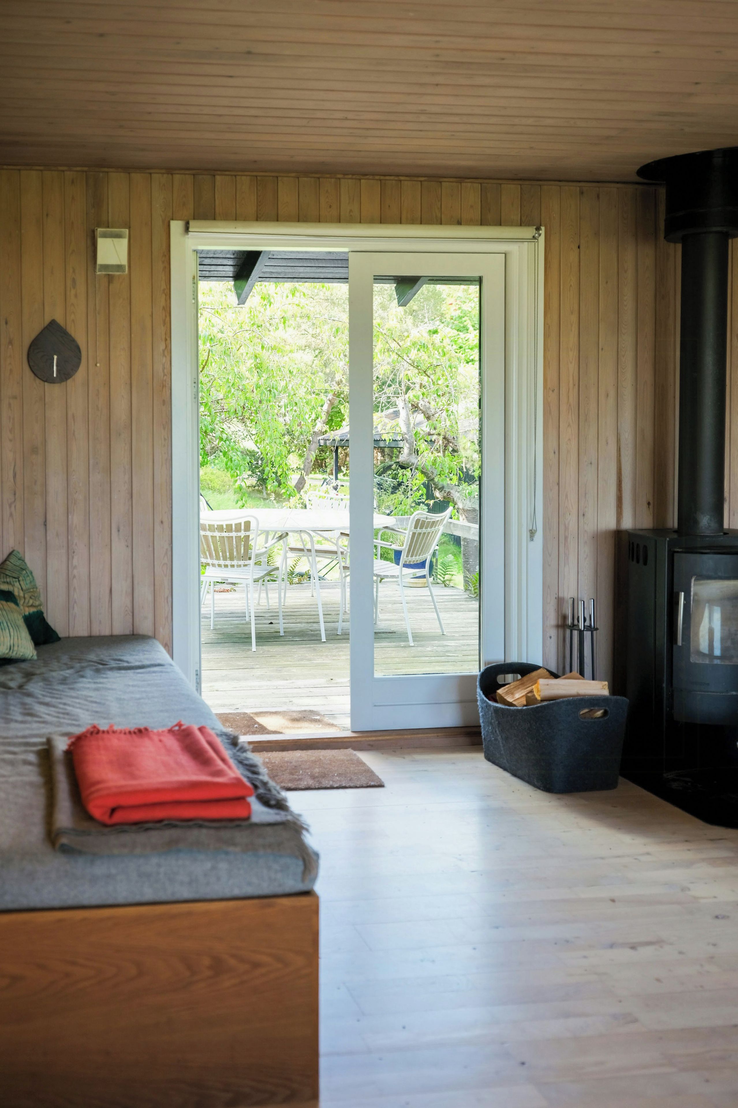 Habitación con cama, suelo de madera, puerta corrediza de vidrio que da a un área exterior con mesa y sillas, y estufa de leña.