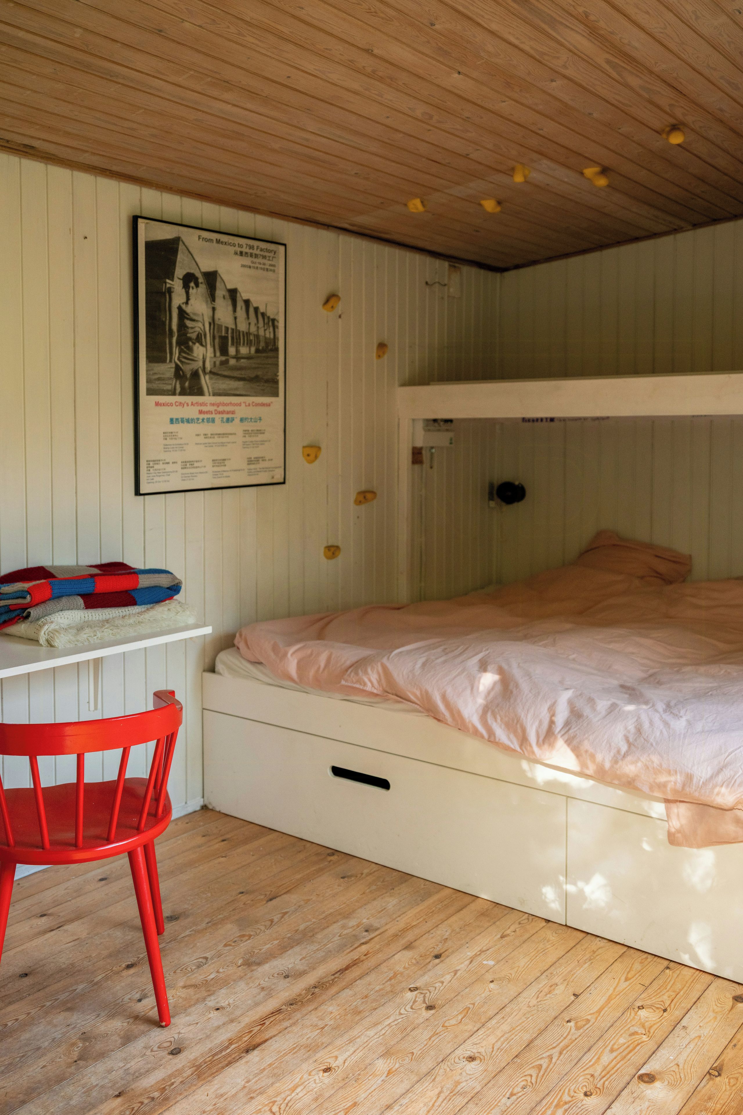 Ein Schlafraum mit Etagenbett, Holzboden, einem roten Stuhl und einem Poster an der Wand.