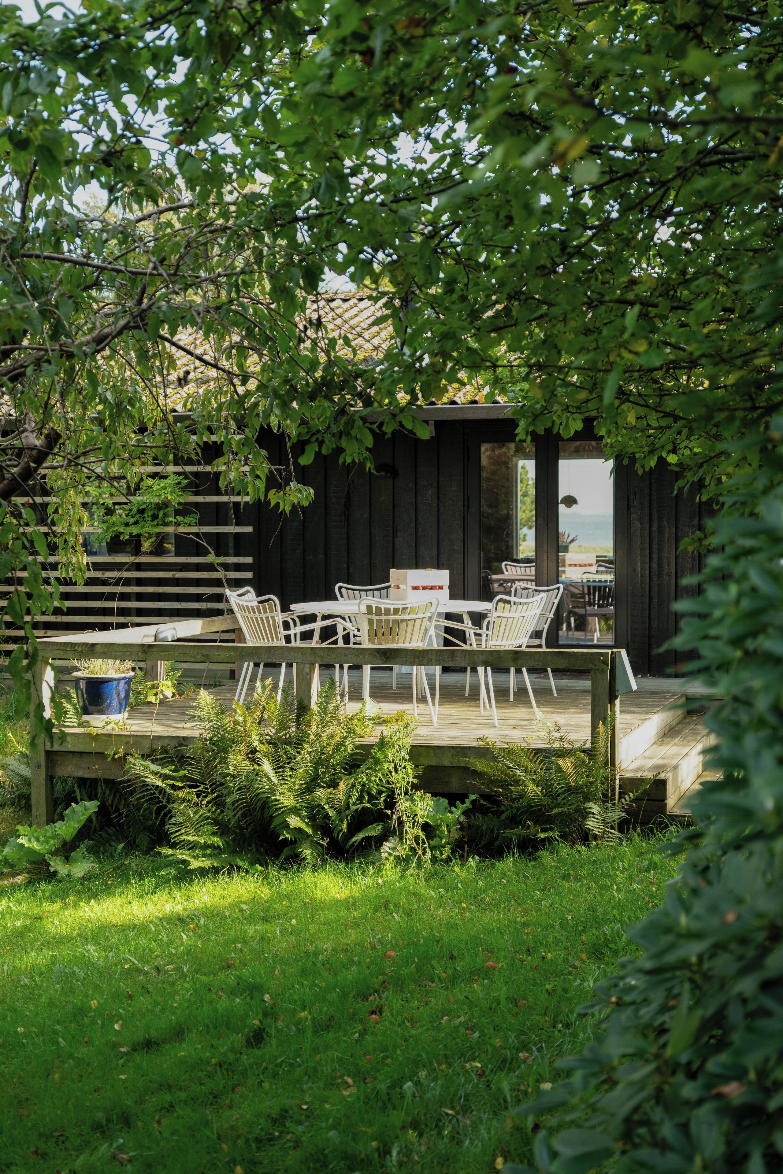 An outdoor seating area with a wooden deck, white metal chairs, and a table.