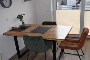 A dining area with a wooden table, two chairs, a clock on the wall, and a view of the outside. - Holiday apartment in Büsum with swimming pool (Büsum)