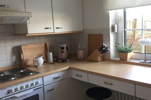 Eine Küche mit weißen Schränken, einer Holz Arbeitsplatte, einem Herd, einer Kaffeemaschine und einem Fenster mit Blick nach draußen.