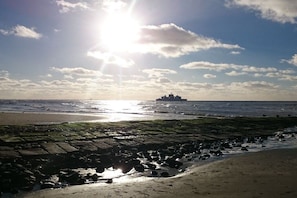 Una playa con un primer plano rocoso, una orilla arenosa y un barco a lo lejos.