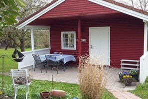 A red wooden building with a covered patio, a table with chairs, and a 'WELCOME' sign. - Holiday home in Sörup with swimming pool (Sörup)