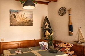 A room with a wooden headboard, a table with a placemat, a wall clock, a decorative wall piece, and a plant in a wire basket. - Holiday apartment with 1 bedroom (Leucate)