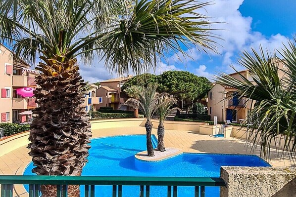 A swimming pool surrounded by palm trees and buildings with balconies. - Holiday apartment with 1 bedroom (Leucate)
