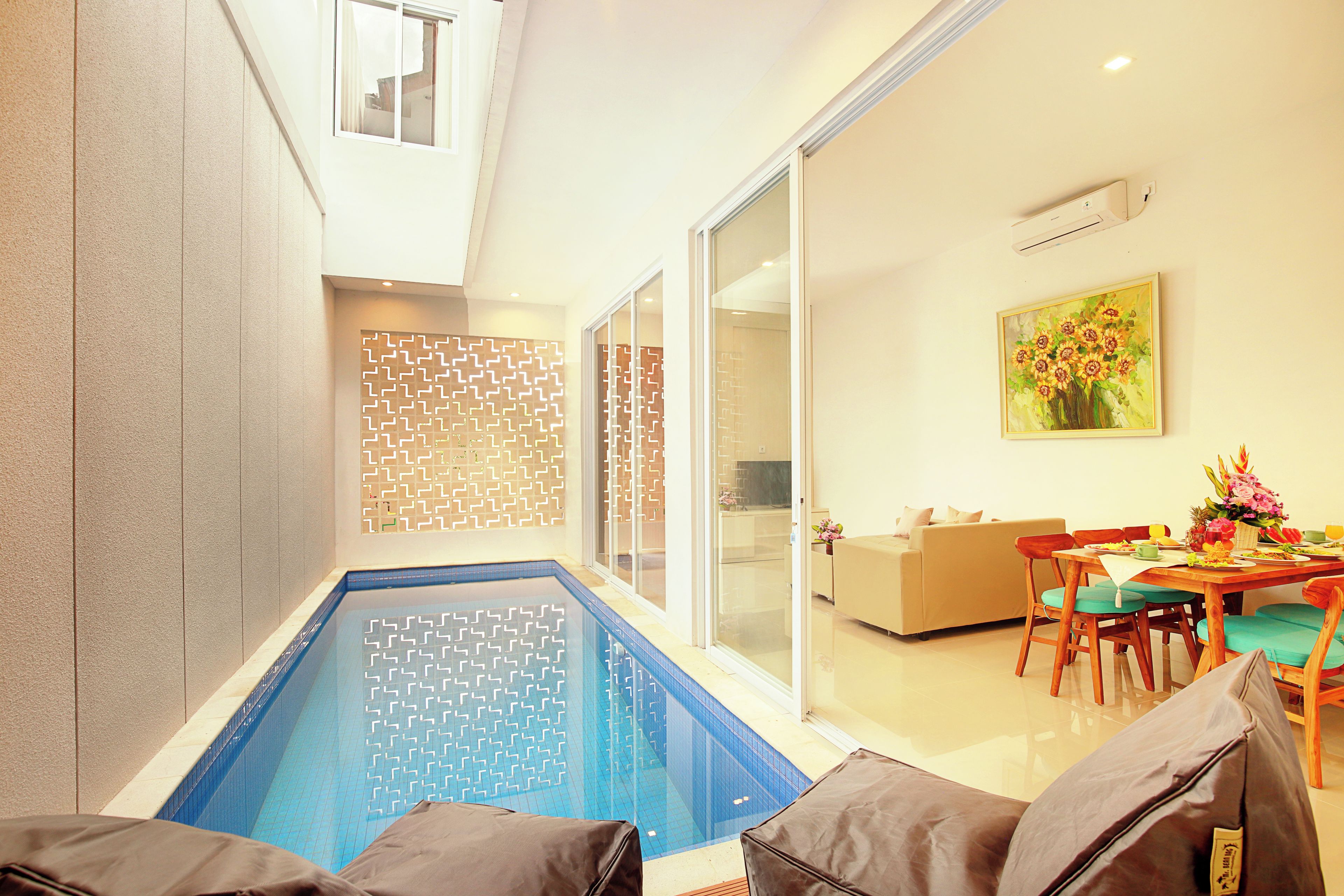 A modern indoor pool with clear blue water, a dining area with a table and chairs, and a sofa.