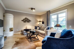 A modern living room with a sofa, armchair, and coffee table. There is a fireplace, a lamp, and a window with curtains. - Holiday home in Sylt with 2 bedrooms (Westerland)