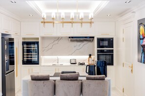 Een moderne keuken met witte kasten, een marmeren spatwand en een centraal kookeiland met zitplaatsen.