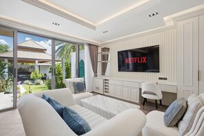 A modern living room with a large flat-screen TV, white sofas, and a view of the outdoors. - 3br Luxurious Villa Gold Chariott (Bangtao)