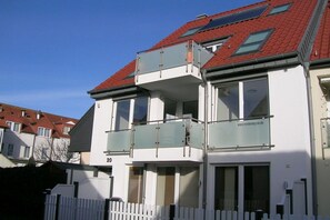 Ein modernes, zweistöckiges Gebäude mit Balkon, großen Fenstern und einem roten Ziegeldach.