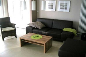 A modern living room with a sofa, a chair, a coffee table, and artwork on the wall. - Holiday apartment with 1 bedroom (Norderney)