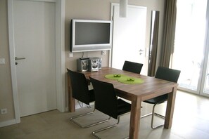 A dining area with a wooden table, four chairs, a television, and a speaker. - Holiday apartment with 1 bedroom (Norderney)