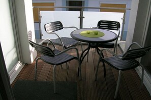 Ein Balkon mit rundem Tisch und vier Stühlen, einer Glastrennwand und Blick auf Gebäude.