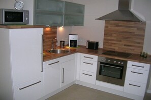 A kitchen with white cabinets, a stainless steel sink, a microwave, a coffee maker, and an oven. - Holiday apartment with 1 bedroom (Norderney)