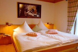 Un lit double avec une literie blanche et deux oreillers, un tableau encadré au mur et une tête de lit en bois.