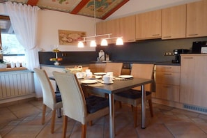 A dining area with a table set for four, surrounded by wicker chairs, in a room with wooden cabinets and a tiled floor. - Sonnenkopf in the country house Alpenglühen (Bolsterlang-Kierwang)