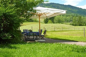 Un espace extérieur aménagé avec une table et des chaises, protégé par un grand parasol, et entouré d’un champ herbeux et d’une clôture.