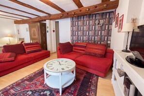 A living room with two red sofas, a white round table, and a bookshelf filled with books. - Holiday apartment with 2 bedrooms (Ribeauville zwischen  Strasbourg und Colmar)