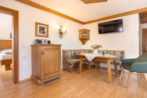 A cozy room with a wooden cabinet, a bench, a table with a vase, and a television mounted on the wall. - Landhaus Pichler holiday apartment Kienberg (Ruhpolding)