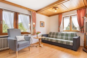 A cozy room with a grey armchair, a plaid sofa, a small wooden table, and a radiator. - Landhaus Pichler holiday apartment Kienberg (Ruhpolding)