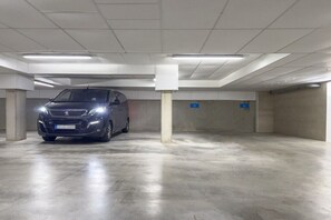 A parking garage with a car parked in a spot, concrete pillars, and fluorescent lighting. - Holiday apartment House Finja 322258 (Kühlungsborn)