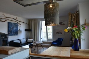 Ein modernes Wohnzimmer mit einem Holztisch, blauen Stühlen, einer Pendelleuchte und einer Blumenvase.